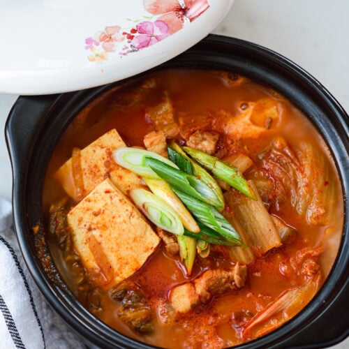 kimchi stew with tofu in an earthen pot with the lid laid on the side of the pot