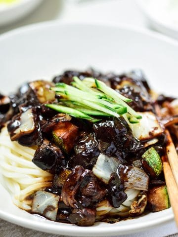 Korean noodles in a black bean sauce topped with cucumber matchsticks and served in a white bowl