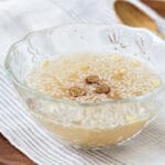 Korean rice drink in a glass bowl with floating grains of rice pine nuts and jujube slices