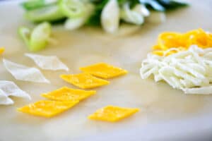 Diamond shaped and thin strips of egg omelette garnish with sliced scallion in the background of cutting board