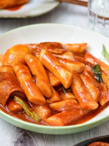 a large bowl of red spicy Korean stir-fried rice cakes with serving plates and chopsticks