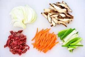 cut beef, mushrooms, onion, carrot, and spring onion on a cutting board