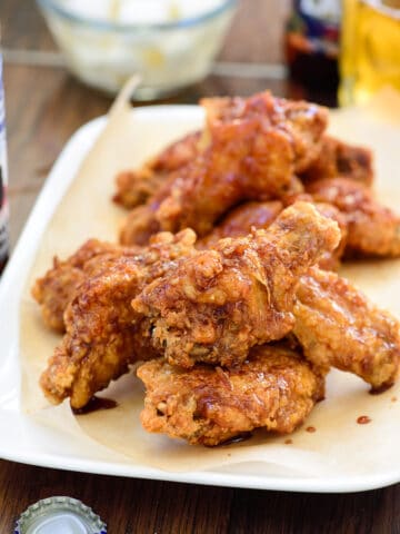 Korean fried chicken glazed with mild and spicy sauces served in a rectangle plate with beer and radish pickles