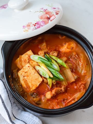 kimchi stew with tofu in an earthen pot with the lid laid on the side of the pot