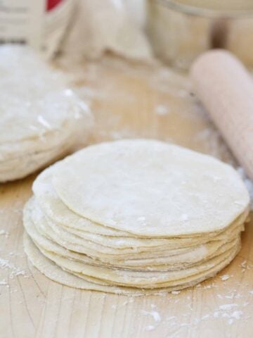 a stack of homemade dumpling wrappers on a wooden cutting board