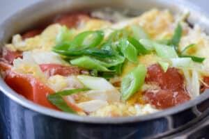 soft tofu and egg soup with tomato and scallions in a pot