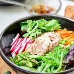 Bibimbap in a large dark color bowl with canned tuna on top with colorful spring vegetables