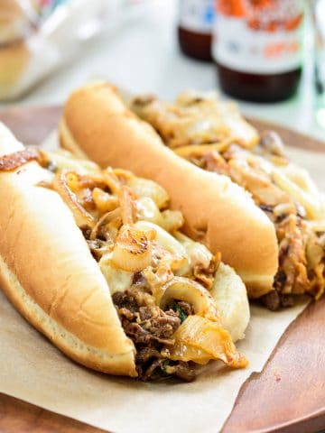 two bulgogi cheese steaks on hoagie buns with beer bottles in the background