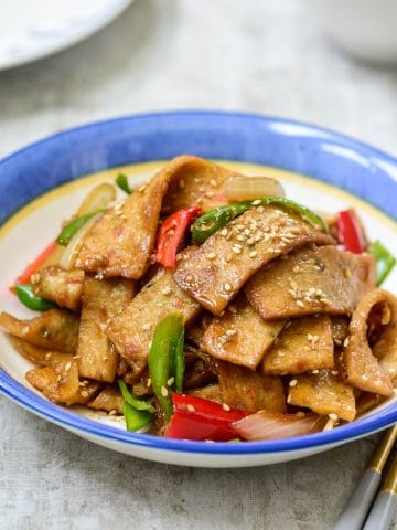 Korean stir-fried fish cakes in small rectangles with green and red pepper slices in a blue rim bowl