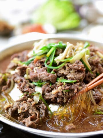 Bulgogi cooked on a Korean tabletop grill pan with glass noodles, scallions and enoki mushrooms