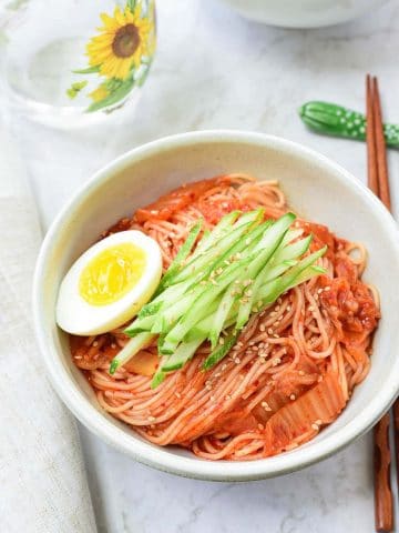 Red spicy cold noodles with kimchi, cucumber match sticks and a half of boiled egg on top